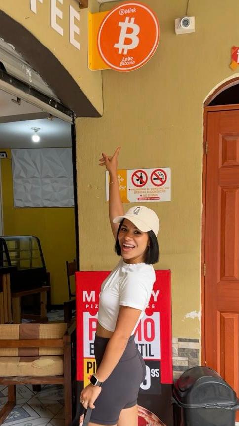 Anuja pointing up at a 'Bitcoin accepted here' sign outside a cafe